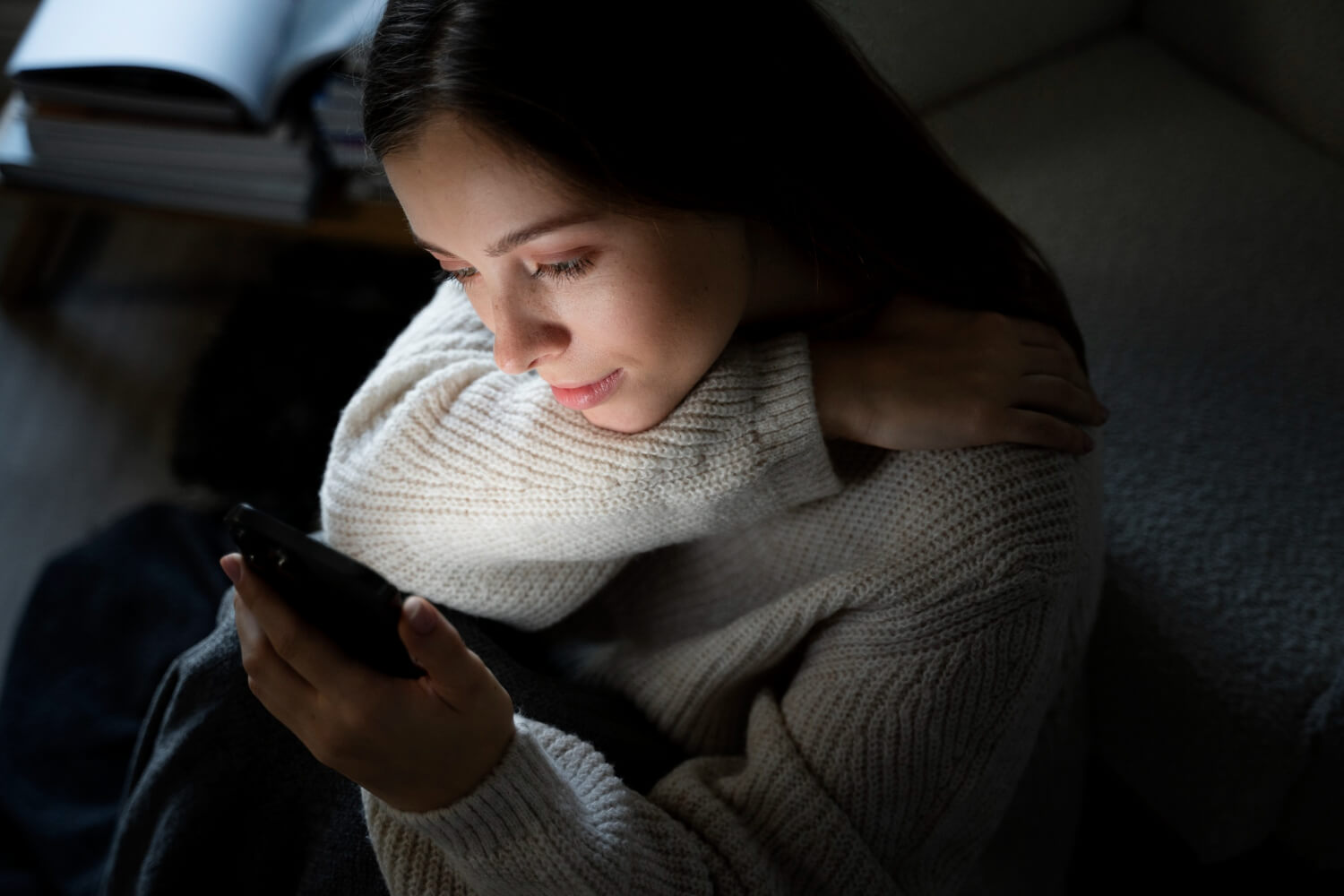 Une personne seule dans une pièce sombre, éclairée uniquement par l'écran de son smartphone.