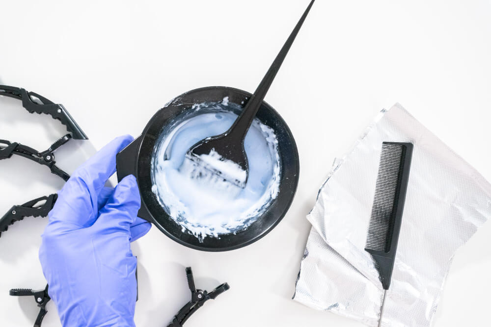 Quel dosage pour réussir ses mèches blondes maison ? 4 Coiffeur mélangeant de la poudre décolorante bleue et de l'oxydant crème dans un bol de coloration.