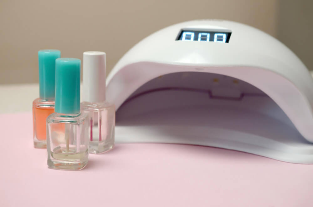 Peut-on sécher un vernis normal avec une lampe LED/UV ? 2 Bouteille de vernis à ongles classique à côté d'une lampe LED UV pour manucure.