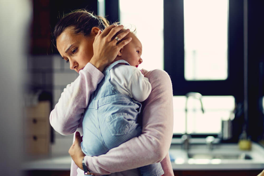 Jeune maman tenant son bébé dans les bras et parlant avec une expression soucieuse à sa belle-mère.