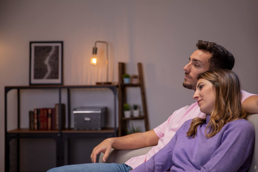 Je suis bien avec elle, mais pas amoureux : que faire ? 2 Homme et femme sur un canapé, la femme sourit et l'homme a l'air pensif et distant.