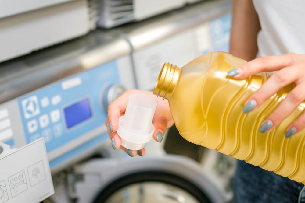 Quel dosage d'eau de Javel pour blanchir le linge sans l'abîmer ? 1 Gobelet doseur versant une petite quantité d'eau de Javel dans le bac dédié d'une machine à laver.