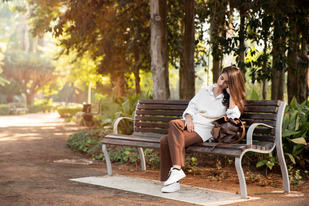 Personne assise seule sur un banc dans un parc, regardant le paysage avec une expression sereine.
