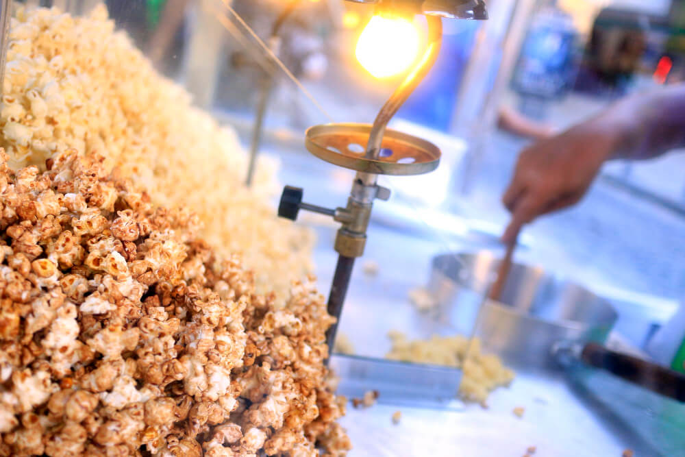 Pop-corn sucré et caramélisé dans un bol à côté d'une machine à pop-corn à air chaud.