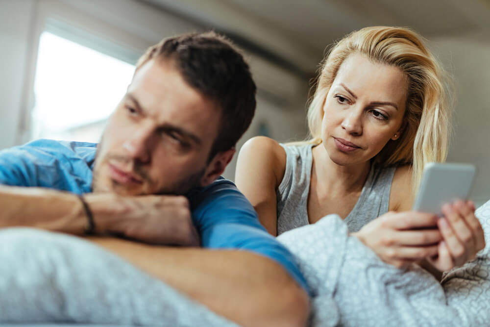 Pourquoi me trompe-t-il mais reste avec moi ? 1 Femme pleurant, assise sur un lit, tandis qu'un homme lui tourne le dos au téléphone.