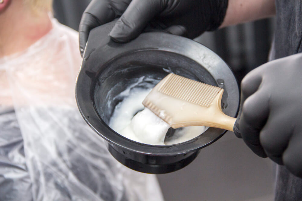 Coiffeur mélangeant de la poudre décolorante bleue et de l'oxydant crème dans un bol de coloration.