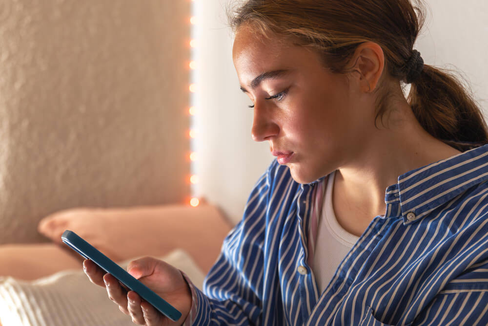 Femme déçue regardant son téléphone après avoir reçu un message d'annulation de rendez-vous.