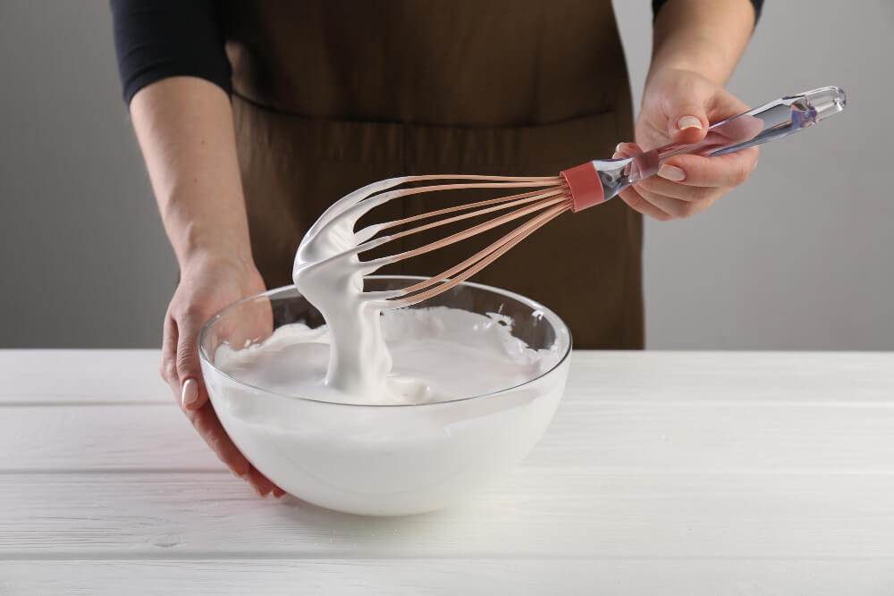 Fouet de pâtisserie dans un bol contenant une meringue liquide et retombée.