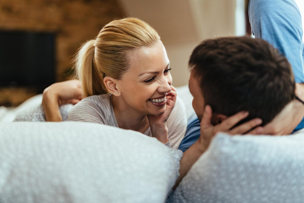Un couple complice partageant un moment de rire et de tendresse sur un canapé pour renforcer leur lien.