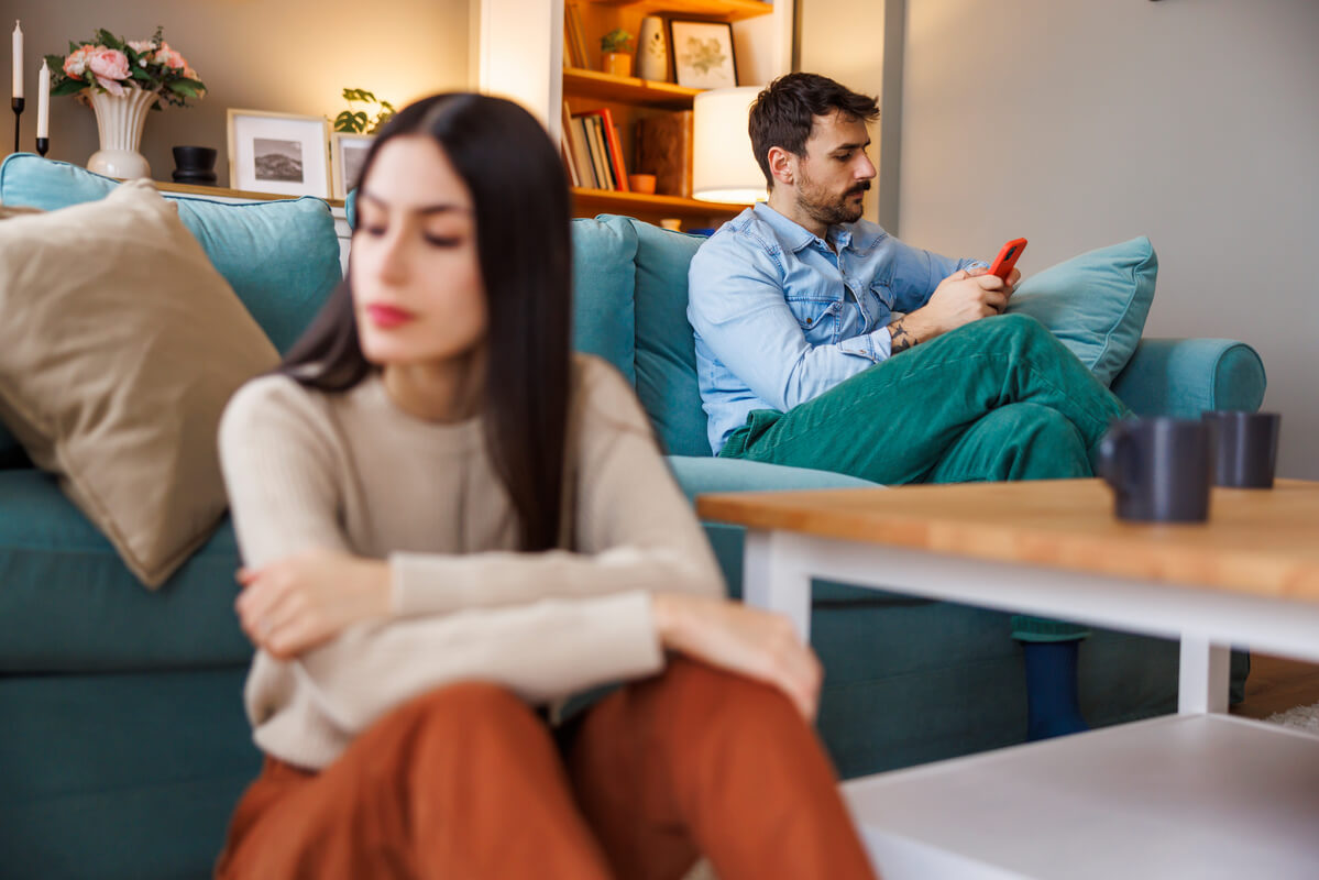 Femme anxieuse observant le smartphone de son partenaire posé sur la table du salon