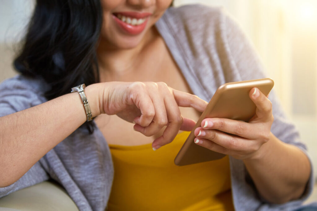 Gros plan sur des mains tapant un SMS bienveillant sur l'écran d'un smartphone.