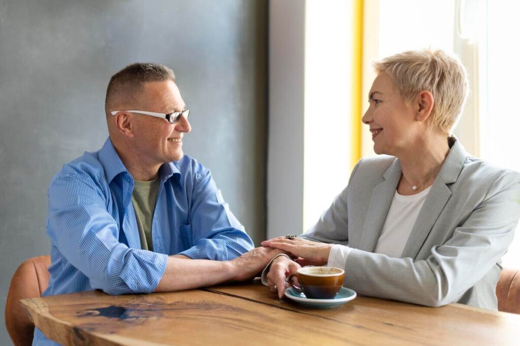 Deux adultes mûrs se rencontrant chaleureusement dans un café, illustrant les retrouvailles après plusieurs décennies.