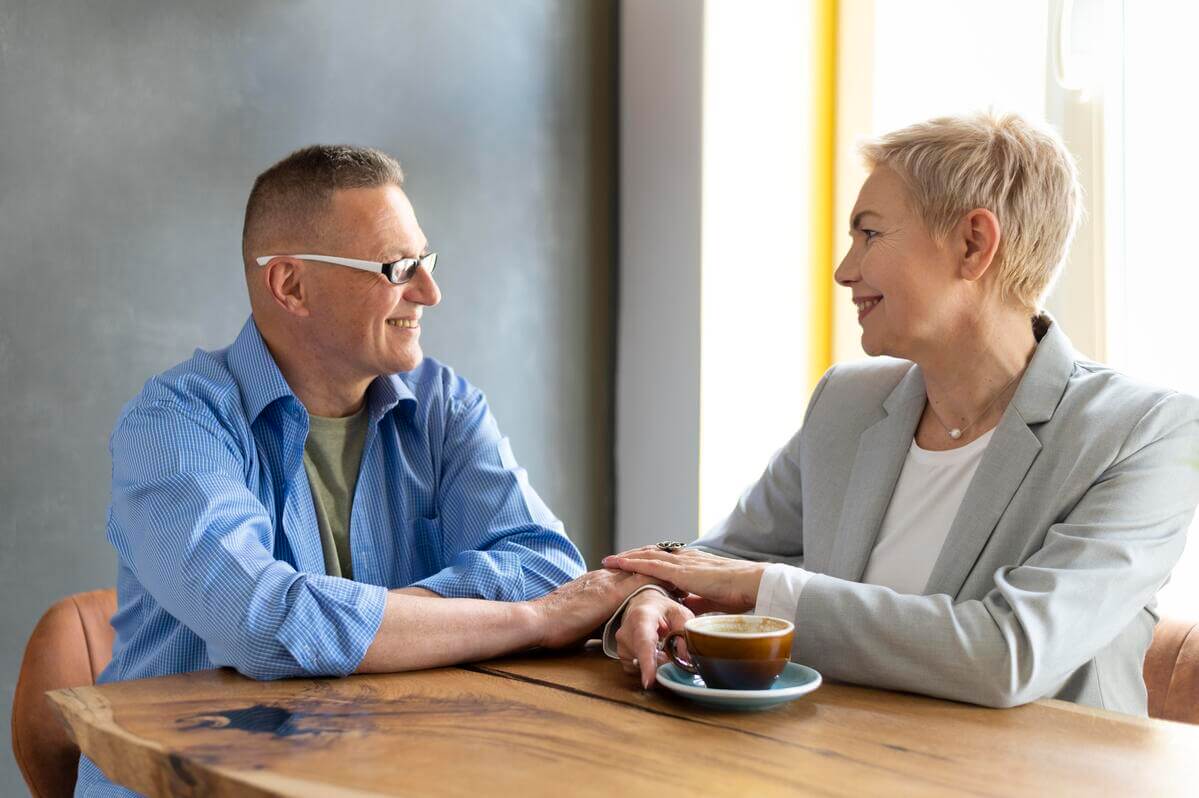 Deux adultes mûrs se rencontrant chaleureusement dans un café, illustrant les retrouvailles après plusieurs décennies.