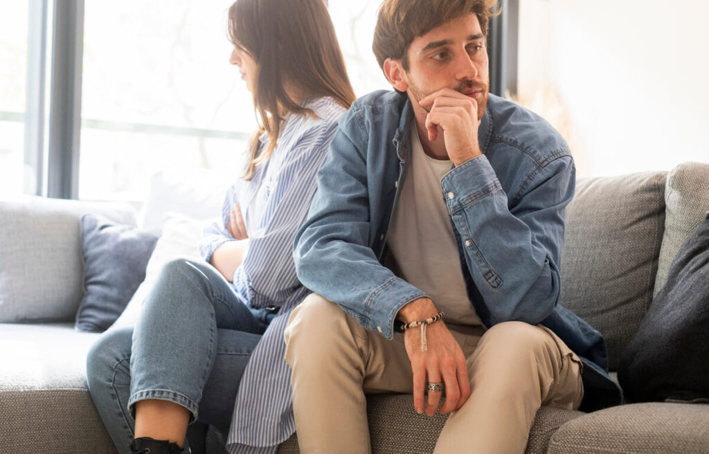 Un couple assis sur un canapé, dos à dos, illustrant une période de doute et de questionnement amoureux.