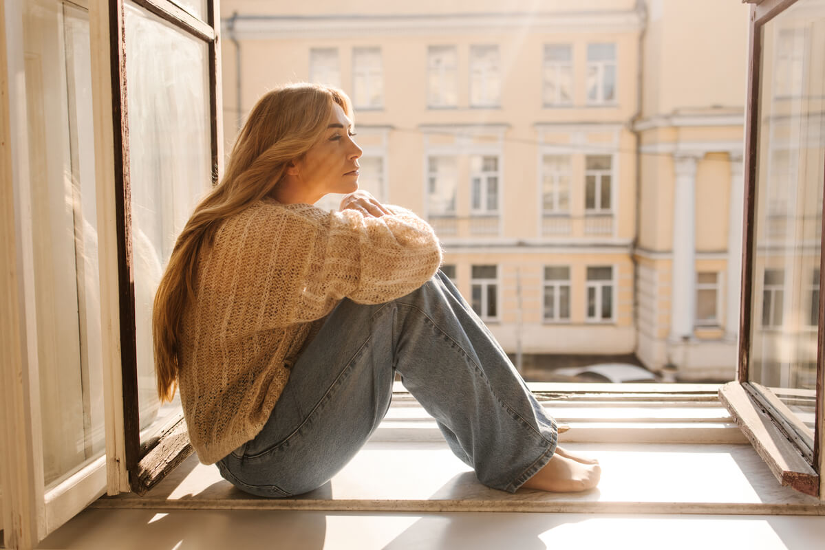 Une personne assise face à une fenêtre, pensive et un peu perdue, illustrant la crise de l'éveil.