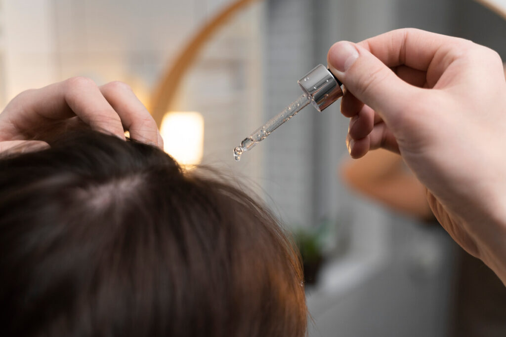 Application d'un sérum capillaire stimulant à la pipette sur la raie des cheveux pour fortifier la repousse.