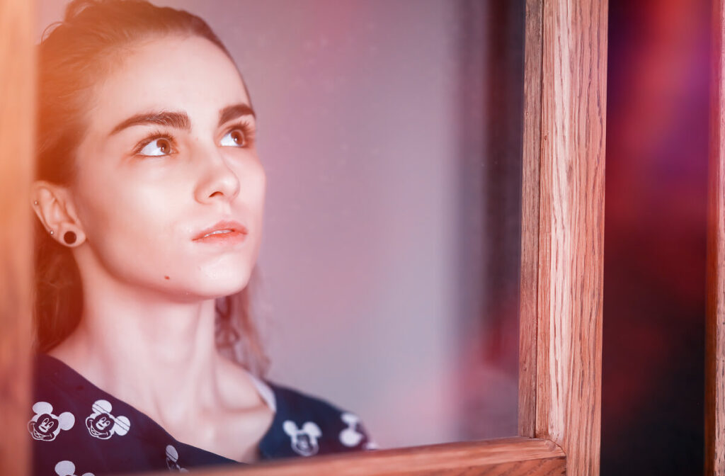 J'ai refait ma vie mais mon ex me manque : que faire ? 2 Une personne pensive regardant par la fenêtre, symbolisant la nostalgie d'un amour passé malgré une nouvelle vie stable.
