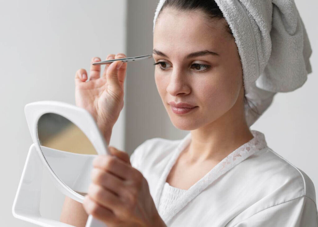 Une femme observant la ligne de ses sourcils et appliquant un soin fortifiant pour accélérer la repousse.