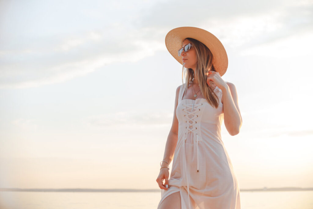 Une femme portant une robe longue bohème chic en dentelle blanche sur une plage au coucher du soleil.