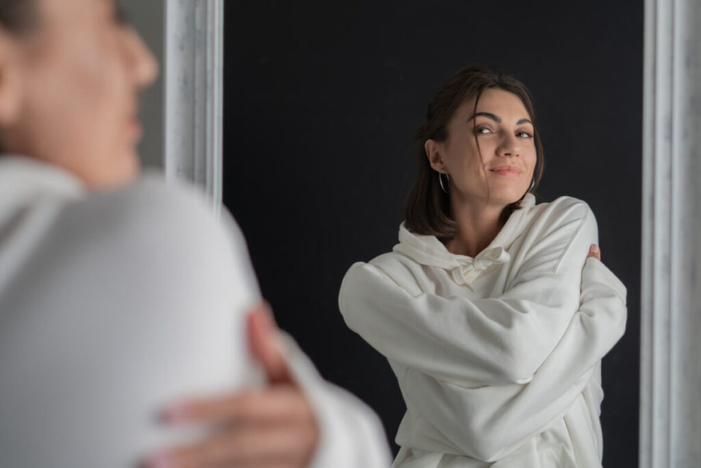 Une femme se regardant dans un miroir avec un sourire serein, symbolisant l'acceptation de soi.