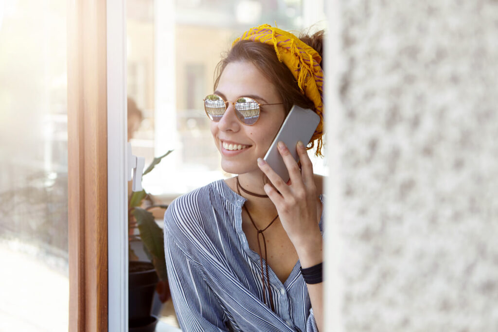 Une personne souriante téléphonant avec son smartphone depuis une ruelle ensoleillée.