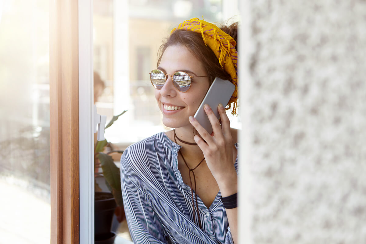 Une personne souriante téléphonant avec son smartphone depuis une ruelle ensoleillée.