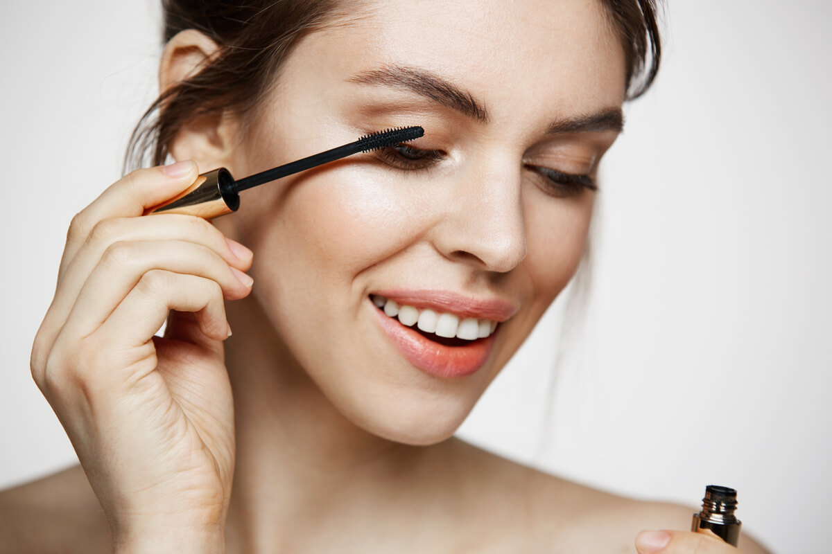 Une femme appliquant délicatement du mascara noir sur ses cils à l'aide d'une brosse applicatrice.