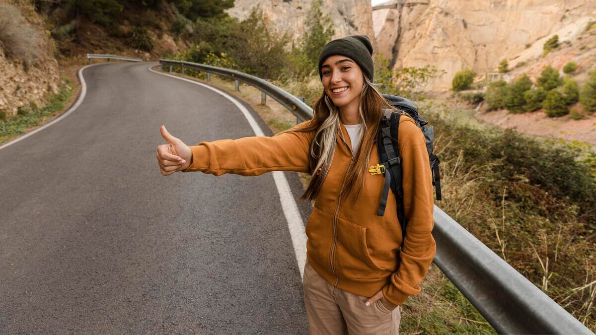 Un voyageur avec son sac à dos levant le pouce au bord d'une route nationale en Espagne.