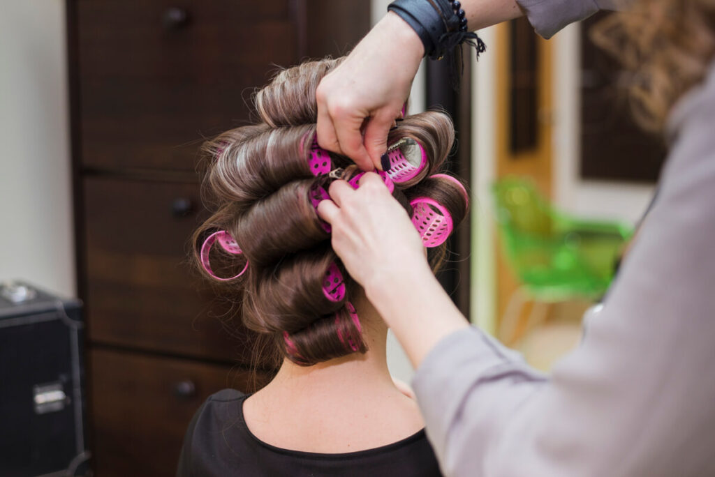 Un coiffeur enroulant de longues mèches de cheveux autour de rouleaux en salon de coiffure.