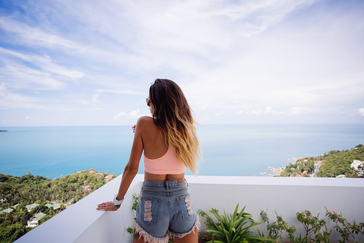 Une personne de dos contemplant la mer depuis une terrasse ensoleillée en Espagne.