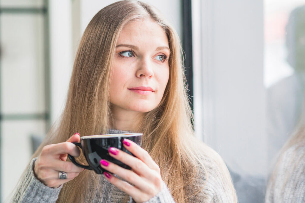 Une femme pensive tenant sa tasse de café en réfléchissant à sa relation.