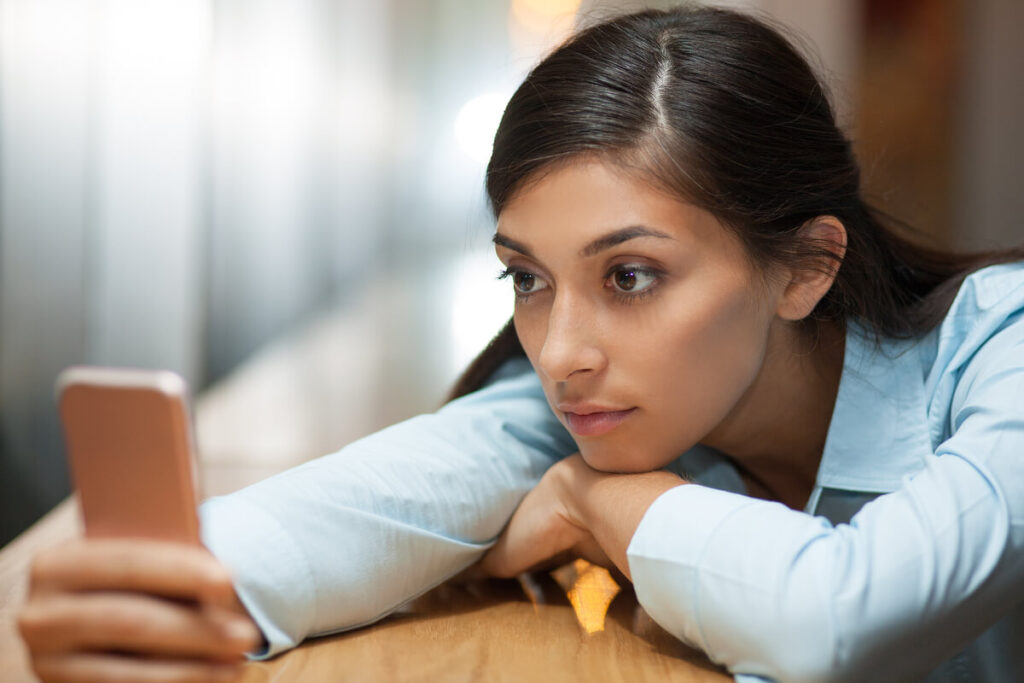 Il parle de moi à son entourage : que signifie ce signe ? 4 Une jeune femme pensive regardant son téléphone, s'interrogeant sur les intentions d'un homme.