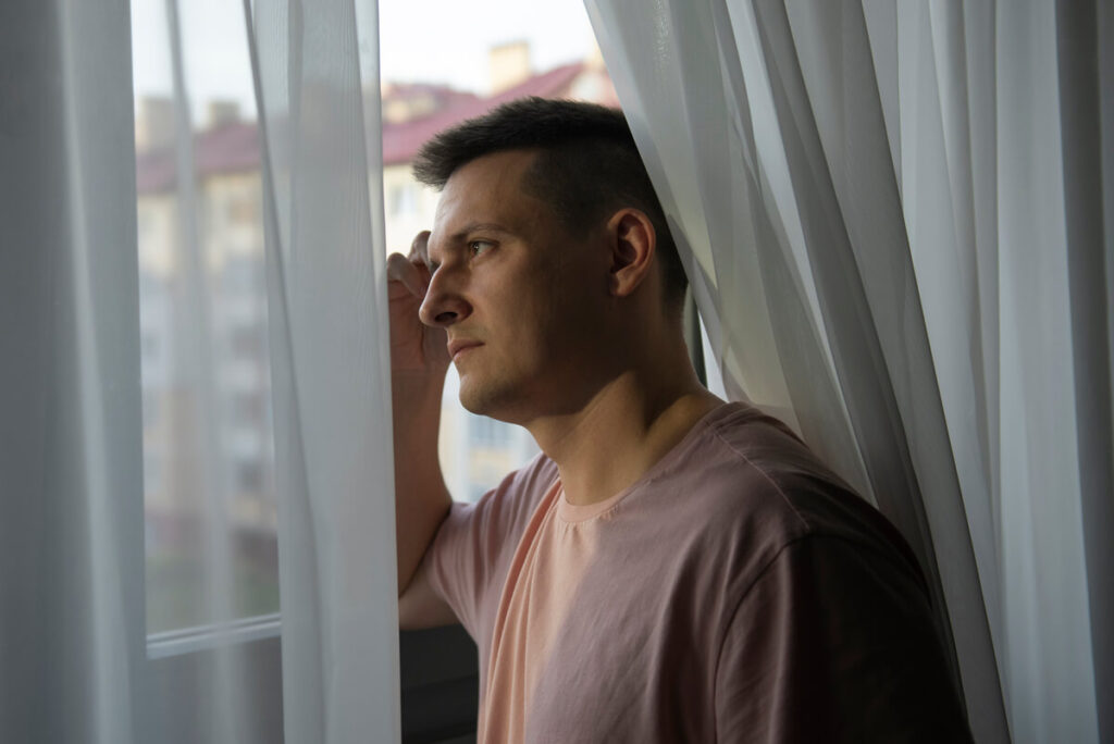 Un homme pensif regardant par la fenêtre en pleine réflexion sur sa vie de couple.