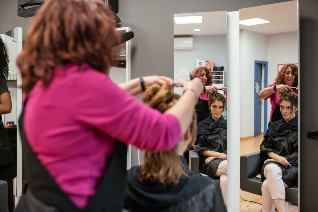 La mini-vague permanente : la technique pour des boucles souples et naturelles 3 Une coiffeuse installant des rouleaux de grand diamètre sur les cheveux d'une cliente en salon.