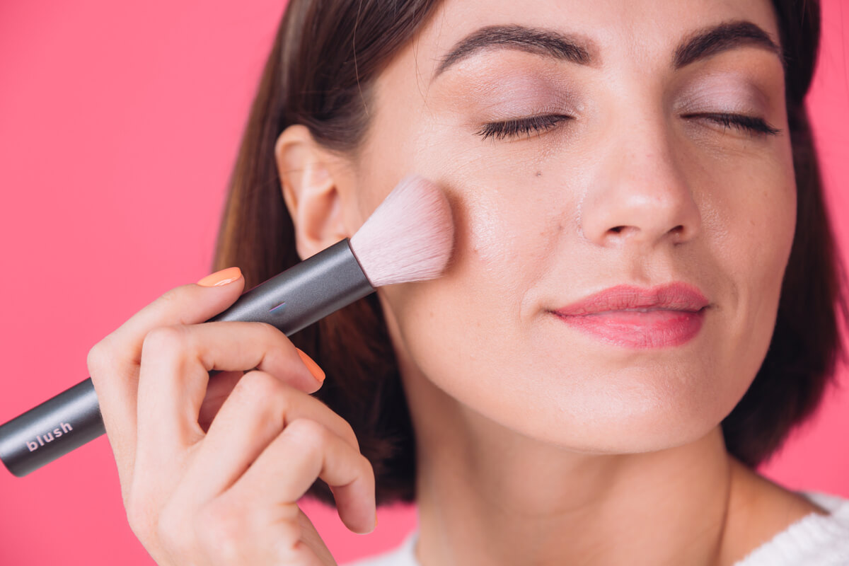 Personne appliquant du fard sur son visage avec un pinceau de maquillage comme une touche de peinture.