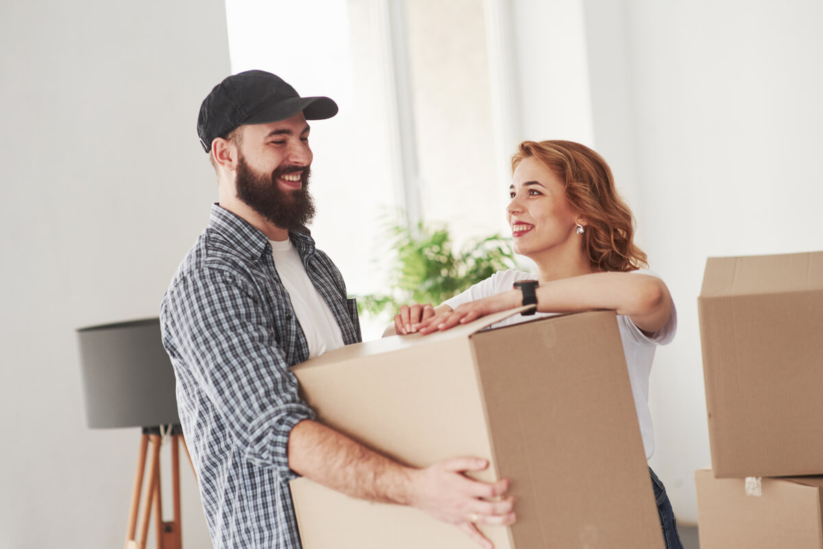 Couple souriant déballant des cartons de déménagement dans leur premier appartement commun.