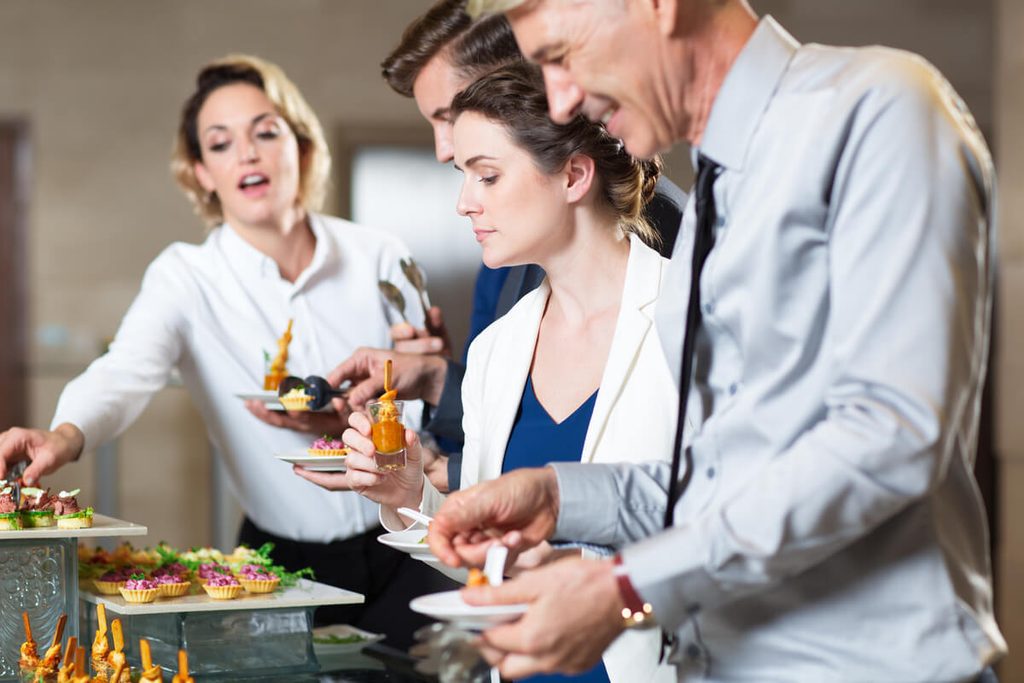 Paella pour un mariage : organisation, quantités et budget 3 Invités de mariage se servant au buffet autour d'une grande poêle à paella conviviale.