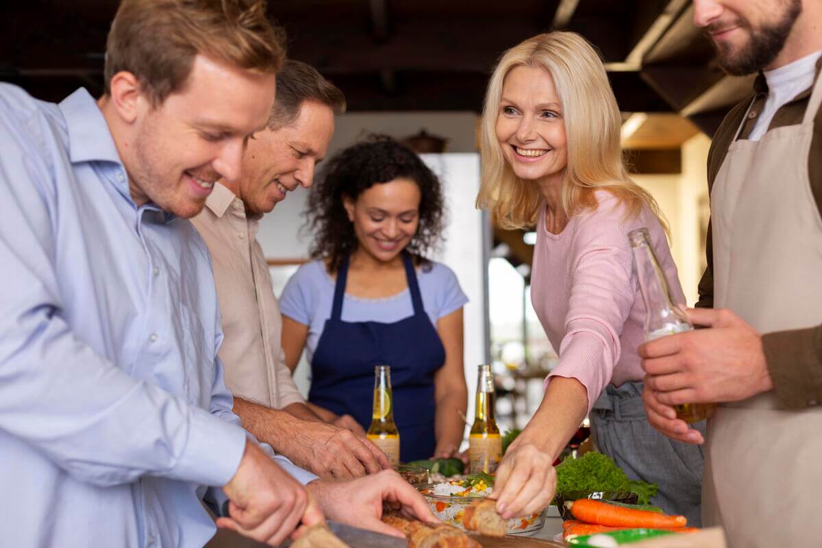 Équipe de collaborateurs souriants préparant un repas ensemble lors d'un atelier culinaire en entreprise.
