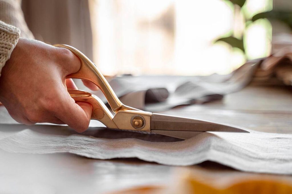 Ciseaux de tailleur découpant un coupon de tissu le long d'un patron de vêtement sur une table d'atelier.