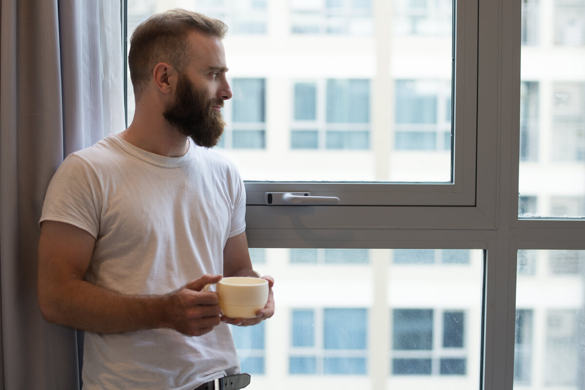Homme songeur regardant par la fenêtre, partagé entre affection et manque d'amour.