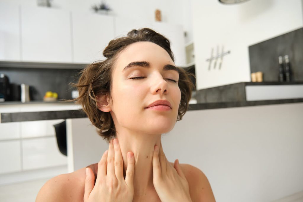Collier qui s'emmêle : signification spirituelle et explication réelle 4 Femme posant la main sur son chakra de la gorge en état de relaxation.