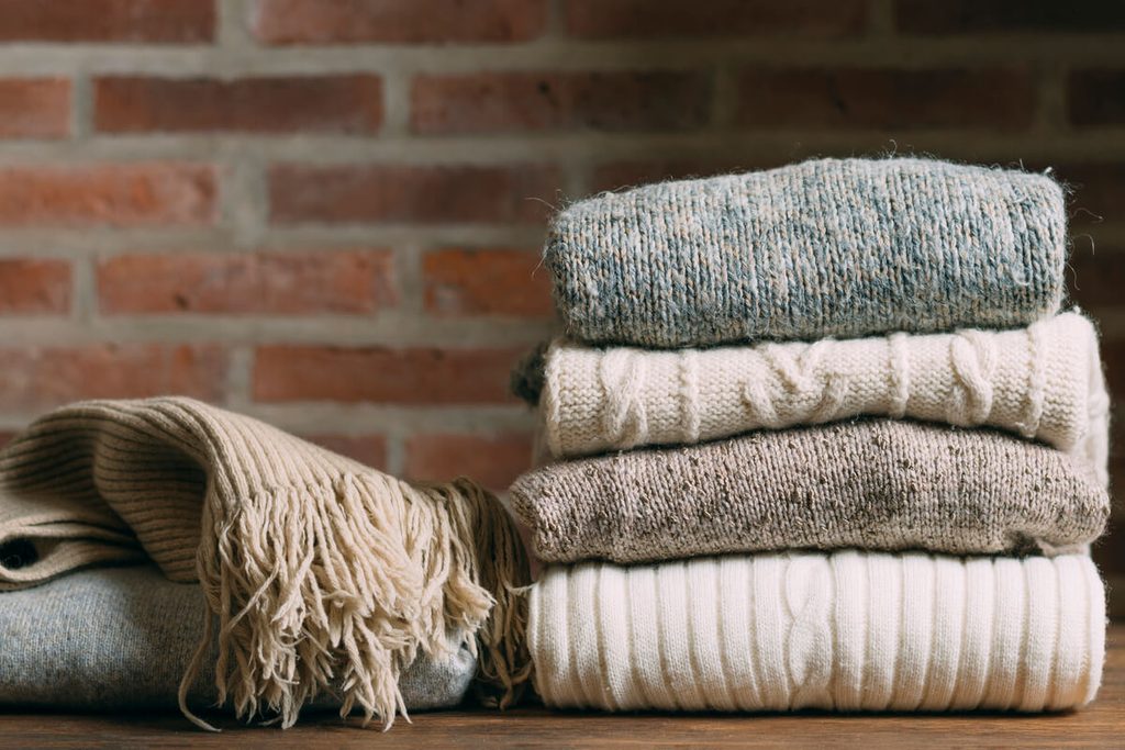 Pile de pulls moelleux en laine et cachemire soigneusement pliés lors de l'organisation d'un dressing d'hiver.